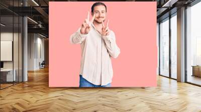 Young handsome caucasian man wearing casual clothes smiling looking to the camera showing fingers doing victory sign. number two. Wall mural