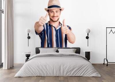 Young handsome caucasian man wearing summer hat approving doing positive gesture with hand, thumbs up smiling and happy for success. winner gesture. Wall mural