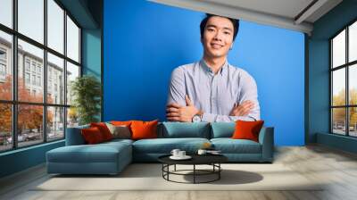 Young handsome chinese man wearing casual shirt standing over isolated blue background happy face smiling with crossed arms looking at the camera. Positive person. Wall mural