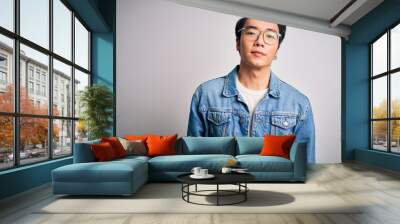 Young handsome chinese man wearing denim jacket and glasses over white background Relaxed with serious expression on face. Simple and natural looking at the camera. Wall mural