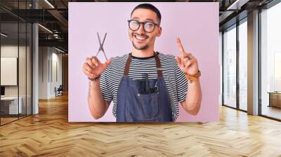 Young handsome hairdresser man wearing apron over pink isolated background surprised with an idea or question pointing finger with happy face, number one Wall mural