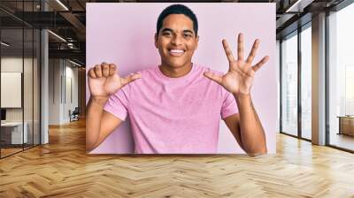 Young handsome hispanic man wearing casual pink t shirt showing and pointing up with fingers number six while smiling confident and happy. Wall mural