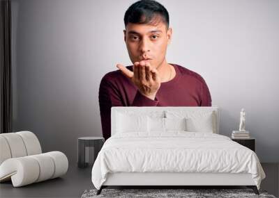 Young handsome hispanic man wearing casual shirt standing over white isolated background looking at the camera blowing a kiss with hand on air being lovely and sexy. Love expression. Wall mural