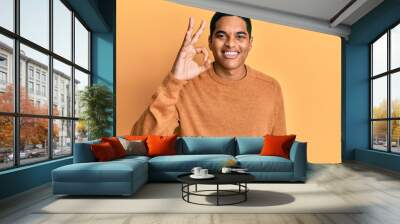 Young handsome hispanic man wearing casual winter sweater smiling positive doing ok sign with hand and fingers. successful expression. Wall mural