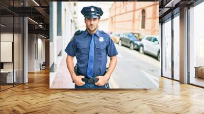 young handsome hispanic policeman wearing police uniform. Standing with serious expression at town street. Wall mural