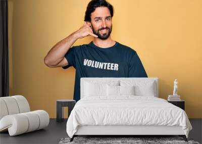 Young handsome hispanic volunteer man wearing volunteering t-shirt as social care smiling doing phone gesture with hand and fingers like talking on the telephone. Communicating concepts. Wall mural