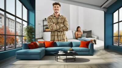 Young handsome man at the living room with girlfriend happy face smiling with crossed arms looking at the camera. positive person. Wall mural