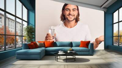 Young handsome man drinking glass of water celebrating achievement with happy smile and winner expression with raised hand Wall mural