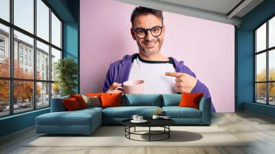 Young handsome man drinking pink mug of coffe standing over isolated background with surprise face pointing finger to himself Wall mural