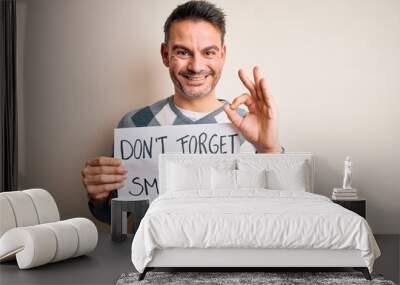 Young handsome man holding banner with funny positive message over white background doing ok sign with fingers, excellent symbol Wall mural