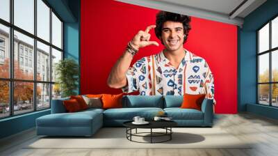 Young handsome man on vacation wearing summer shirt over isolated red background smiling and confident gesturing with hand doing small size sign with fingers looking and the camera. Measure concept. Wall mural