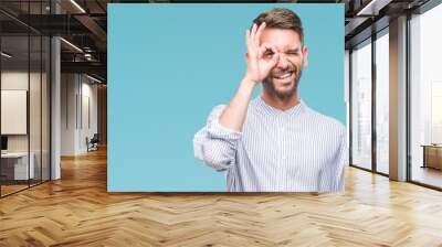 Young handsome man over isolated background doing ok gesture with hand smiling, eye looking through fingers with happy face. Wall mural