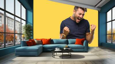 Young handsome man over isolated background very happy and excited doing winner gesture with arms raised, smiling and screaming for success. Celebration concept. Wall mural