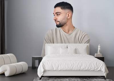 Young handsome man standing over isolated background looking to the side with arms crossed convinced and confident Wall mural