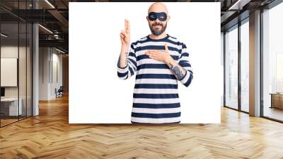 Young handsome man wearing burglar mask smiling swearing with hand on chest and fingers up, making a loyalty promise oath Wall mural