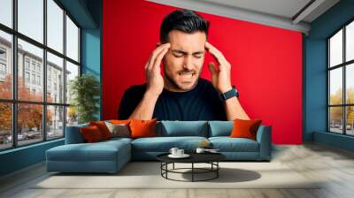 Young handsome man wearing casual black t-shirt standing over isolated red background with hand on head for pain in head because stress. Suffering migraine. Wall mural