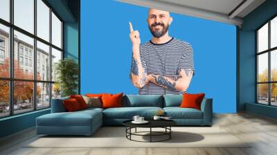 Young handsome man wearing casual clothes with a big smile on face, pointing with hand and finger to the side looking at the camera. Wall mural