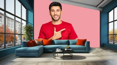 Young handsome man wearing casual red tshirt cheerful with a smile on face pointing with hand and finger up to the side with happy and natural expression Wall mural