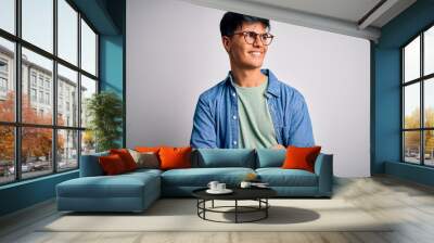 Young handsome man wearing casual shirt and glasses over isolated white background looking away to side with smile on face, natural expression. Laughing confident. Wall mural