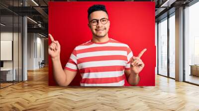 Young handsome man wearing casual striped t-shirt and glasses over isolated red background smiling confident pointing with fingers to different directions. Copy space for advertisement Wall mural