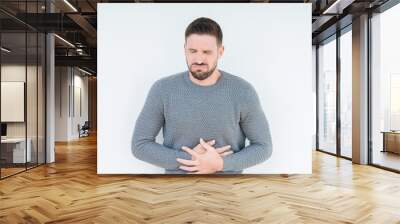 Young handsome man wearing casual sweater over isolated background with hand on stomach because nausea, painful disease feeling unwell. Ache concept. Wall mural