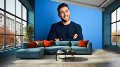 Young handsome man wearing casual sweater standing over isolated blue background happy face smiling with crossed arms looking at the camera. Positive person. Wall mural