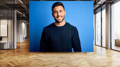 Young handsome man wearing casual sweater standing over isolated blue background with a happy and cool smile on face. Lucky person. Wall mural