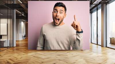 Young handsome man wearing casual sweater standing over isolated pink background pointing finger up with successful idea. Exited and happy. Number one. Wall mural