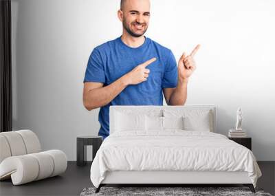 Young handsome man wearing casual t shirt smiling and looking at the camera pointing with two hands and fingers to the side. Wall mural