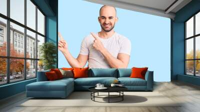 Young handsome man wearing casual t shirt smiling and looking at the camera pointing with two hands and fingers to the side. Wall mural