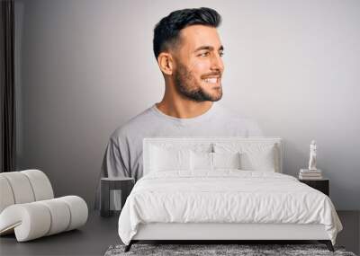 Young handsome man wearing casual t-shirt standing over isolated white background looking away to side with smile on face, natural expression. Laughing confident. Wall mural