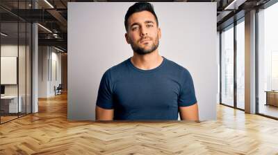 Young handsome man wearing casual t-shirt standing over isolated white background Relaxed with serious expression on face. Simple and natural looking at the camera. Wall mural