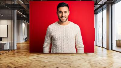 Young handsome man wearing casual white sweater standing over isolated red background with a happy and cool smile on face. Lucky person. Wall mural