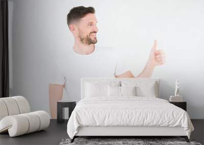 Young handsome man wearing casual white t-shirt over isolated background Looking proud, smiling doing thumbs up gesture to the side Wall mural