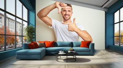 Young handsome man wearing casual white t-shirt over isolated background smiling making frame with hands and fingers with happy face. Creativity and photography concept. Wall mural