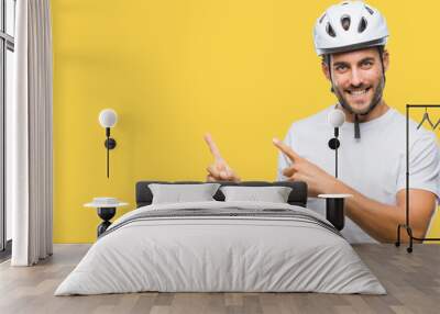 Young handsome man wearing cyclist safety helmet over isolated background smiling and looking at the camera pointing with two hands and fingers to the side. Wall mural