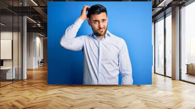 Young handsome man wearing elegant shirt standing over isolated blue background confuse and wonder about question. Uncertain with doubt, thinking with hand on head. Pensive concept. Wall mural