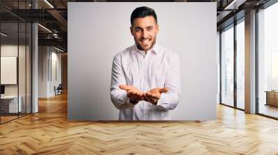 Young handsome man wearing elegant shirt standing over isolated white background Smiling with hands palms together receiving or giving gesture. Hold and protection Wall mural