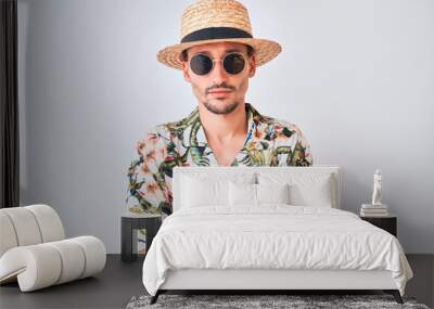 Young handsome man wearing Hawaiian shirt and summer hat over isolated background skeptic and nervous, disapproving expression on face with crossed arms. Negative person. Wall mural