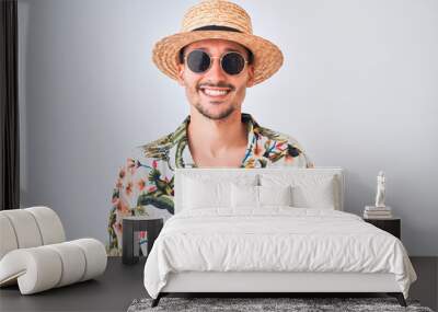 Young handsome man wearing Hawaiian shirt and summer hat over isolated background with a happy and cool smile on face. Lucky person. Wall mural