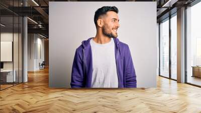 Young handsome man wearing purple sweatshirt standing over isolated white background looking away to side with smile on face, natural expression. Laughing confident. Wall mural