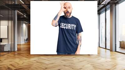 Young handsome man wearing security t shirt doing ok gesture shocked with surprised face, eye looking through fingers. unbelieving expression. Wall mural