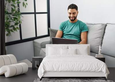 Young handsome man with beard using computer laptop sitting on the sofa at home with a happy and cool smile on face. lucky person. Wall mural