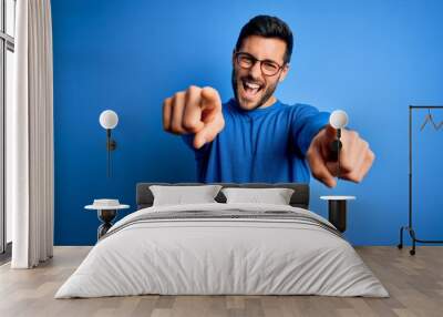 Young handsome man with beard wearing casual sweater and glasses over blue background pointing to you and the camera with fingers, smiling positive and cheerful Wall mural