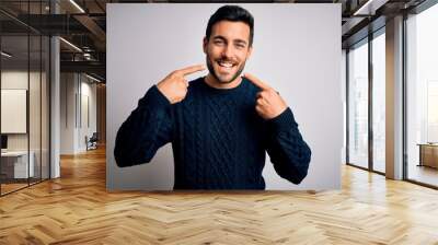 Young handsome man with beard wearing casual sweater standing over white background smiling cheerful showing and pointing with fingers teeth and mouth. Dental health concept. Wall mural