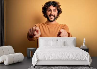 Young handsome man with beard wearing casual sweater standing over yellow background pointing to you and the camera with fingers, smiling positive and cheerful Wall mural