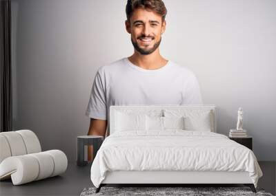 Young handsome man with beard wearing casual t-shirt standing over white background with a happy and cool smile on face. Lucky person. Wall mural