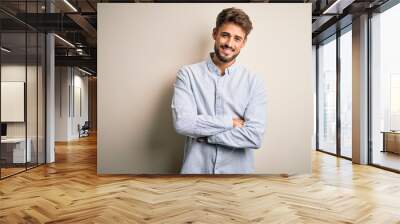 Young handsome man with beard wearing striped shirt standing over white background happy face smiling with crossed arms looking at the camera. Positive person. Wall mural