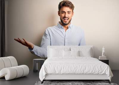 Young handsome man with beard wearing striped shirt standing over white background smiling cheerful with open arms as friendly welcome, positive and confident greetings Wall mural