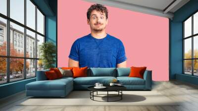 Young handsome man with curly hair wearing casual clothes puffing cheeks with funny face. mouth inflated with air, crazy expression. Wall mural